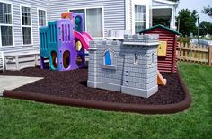 there is a play set in the front yard with grass and mulch on the ground