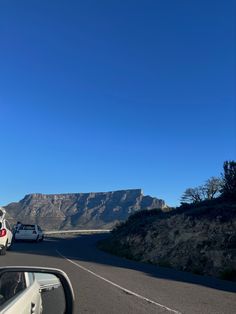 cars are driving down the road in front of some mountains and blue sky with no clouds