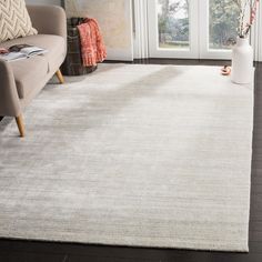 a white rug in a living room next to a couch and chair with a vase on the floor