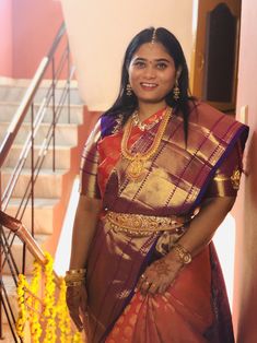 a woman in a red and gold sari standing next to some yellow garlands