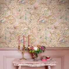 a table with flowers and candles on it in front of a wallpapered background