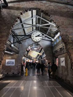 people are walking down an alley way with a clock hanging from the ceiling