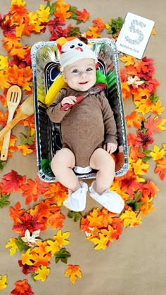 a baby is sitting in a box surrounded by fall leaves and flowers with a spoon