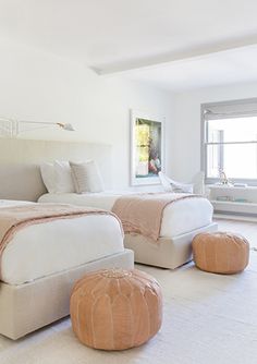 two beds in a room with white walls and flooring, one has an ottoman on the other side