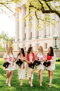 four women in graduation gowns walk through the grass