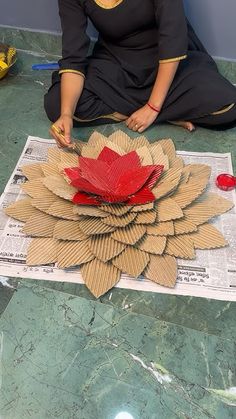 a woman is sitting on the floor making a flower out of cardboard and construction material