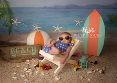 a baby sitting in a chair on the beach wearing sunglasses and holding a toy surfboard