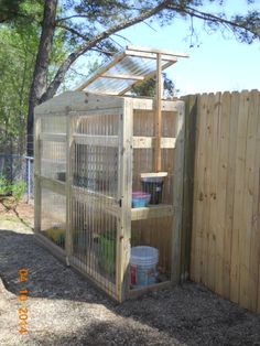 a wooden bird cage in the middle of a fenced off area with buckets