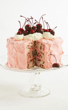 a cake with pink frosting and cherries on top sitting on a glass plate