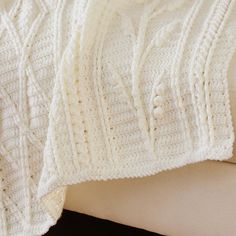 a white crocheted blanket sitting on top of a couch next to a pillow