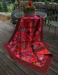 a table and chairs on a deck with a red quilt draped over the top of it