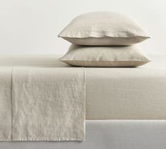 two pillows on top of a bed with white sheets and linens in the background