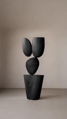 three black vases sitting on top of each other in front of a white wall