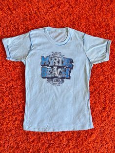 "1970s Myrtle Beach light blue tee with exposed stitching detail, so good! No tag - go by measurements below for best fit. Buyer is responsible for confirming fit and sales are final. Please reach out with any questions!  CONDITION: excellent vintage condition w/ no major wear MEASUREMENTS (taken laying flat then doubled where applicable:) 24\" long  33\" pit to pit - 38\" stretched 30\" waist  14\" shoulder Model is 5'2 34/27/38 for reference Follow us on Instagram for first dibs and special di Blue Retro Tops For Beach Season, Light Wash Cotton Tops For Vacation, Light Blue Short Sleeve Tops For Beach Season, Retro Short Sleeve Tops For Beach Season, Vintage Tops With Letter Print For Beach Season, Vintage Short Sleeve Tops For Beach, Vintage Letter Print Top For Beach Season, Vintage Letter Print Tops For Beach Season, Light Wash Cotton Beach Top