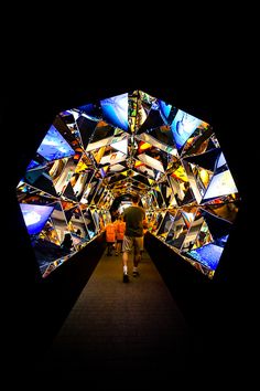 two people walking down a dark tunnel with colorful images on the walls