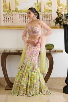 Introducing our Marina Lehenga Set, a mesmerizing Ombre blend adorned with botanical motifs, pastel-hued beads, crystal stones, moti, sequins, and seashell detailing. Paired with a glamorous halter-neck blouse adorned with fine hand embroidery and complemented by a translucent pre-stitched dupatta detailed with tiny sequined flowers. Halter neck blouse with tie-up straps attached with tassels at the back. The blouse contains a back center hook. The blouse embroidered with flower motifs comes with a cut-out detailing at the back. Mermaid-style floor-length skirt embellished with botanical embroidery accentuated with crystals, beads, and sea-shells detailing. Pretty tassel drop attached with strings on the left side of the skirt. Lehenga contains a metal zip on the left side. From Moledro’s Two Layer Lehenga, Ghagra Blouse Back Neck Designs, Dress Hand Embroidery Designs, Carnival Outfit Ideas Indian Wedding, Pestal Colour Lehanga, Stitched Lehenga Ideas, Mermaid Cut Lehenga, Lehenga New Design, Hand Embroidery Lehenga