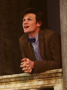 a man in a suit and bow tie sitting on a ledge with his mouth open