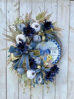 a wreath with blue and white flowers is hanging on a wooden wall, it says welcome fall