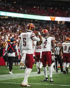 two football players standing on the sidelines during a game with fans in the stands