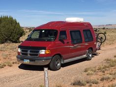 a red van parked on the side of a dirt road next to a bike rack