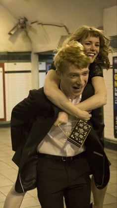 a man carrying a woman on his back in a subway station while they both laugh and hug