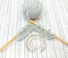 two balls of yarn and knitting needles on a white wooden floor with wood planks