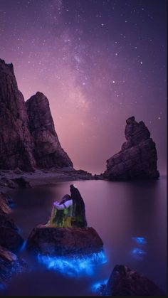 two people are sitting on rocks in the water with their backs to each other and looking up at the night sky