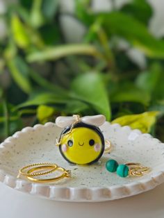 a small yellow smiley face ring sitting on top of a white plate next to green plants