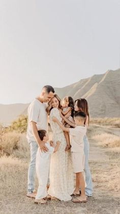 a group of people standing around each other in the middle of an open field with mountains in the background