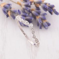 a white gold wedding band with three diamonds on it and lavender flowers in the background