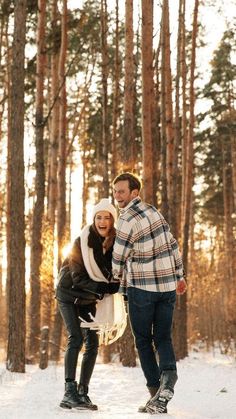 a man and woman standing in the snow next to each other with trees behind them