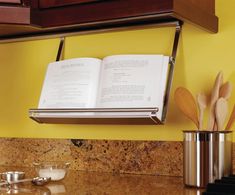 an open book sitting on top of a shelf next to a cup and spoons