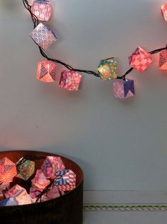 a string of colorful paper cubes hanging from a wall next to a wooden bowl