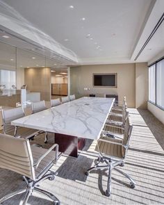 an empty conference room with chairs and a large marble table in the foreground is a flat screen tv