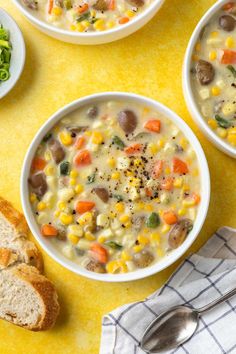 three bowls filled with soup next to bread and vegetables on a yellow tablecloth,