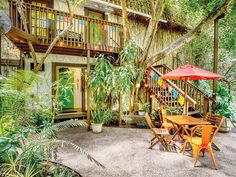 an outdoor patio with tables and chairs under umbrellas in front of a house surrounded by trees