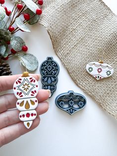 a hand holding three ceramic ornaments on top of a white table next to a plant