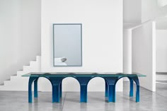 a blue table sitting in the middle of a room next to a white wall and stairs