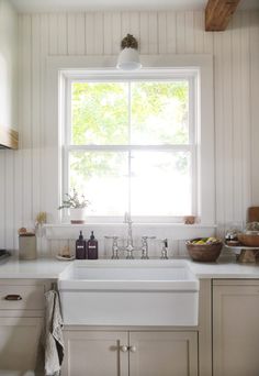 a white kitchen sink sitting under a window in front of a counter top with dishes and utensils on it