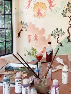 an artist's desk with paint, brushes and paints on it in front of a window