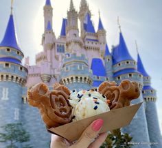 a person holding up an ice cream cone in front of a castle at disney world