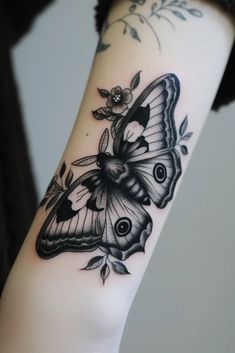 a black and white butterfly tattoo on the left arm, with leaves around it's wings