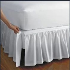 a bed with a white bedspread on top of it and a hand holding the edge of the bed