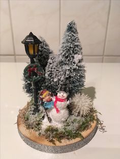 there is a snowman and two children in front of a lamp post on the table