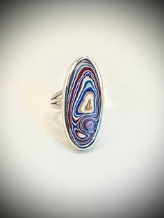 "Genuine Fordite / Detroit Agate set in sterling silver. Bold colors of red, blue and gold swirl with white accents. Exactly what you want to see in a Fordite cabachon. Sterling silver setting is 1-3/8\"  long by 5/8\"  wide. (35mm X 15cm.) Sterling triple-split ring shank makes it easy to wear and provides a linear accent. Fordite is also called \"Detroit Agate.\" It is the result of over-spray in the paint booth in old auto factories. As it built up inside the booth the paint had to be removed from the rails that took the autos through the curing ovens. As new technologies emerged and robots took over the painting any over-spray is now minimal, therefore, Fordite is becoming a rare material. Size 7-1/2. Comes with gift box and cleaning cloth." Vintage Multicolor Agate Jewelry, Handmade Multi-strand Agate Jewelry, Unique Nickel-free Agate Jewelry, Fordite Ring, Sterling Silver Multi-stone Crystal Ring, Oval Shape, Fordite Detroit Agate, Paint Booth, Ring Shank, Agate Ring