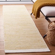 a white rug is on the floor next to a chair and vase with a yellow blanket