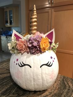 a white pumpkin decorated with flowers and a unicorn's face