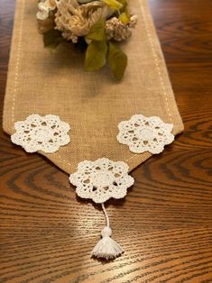 the table runner is decorated with white doily and tassels, along with a bouquet of flowers