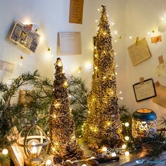 three christmas trees sitting on top of a mantle covered in lights and pineconis