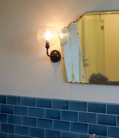 a bathroom sink with a mirror and light on the wall above it, in front of a blue tiled wall